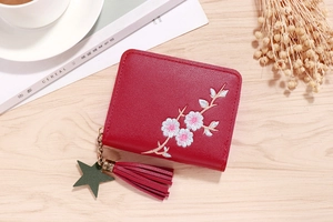 Detail of a dark red short leather wallet featuring floral embroidery and a tassel zipper