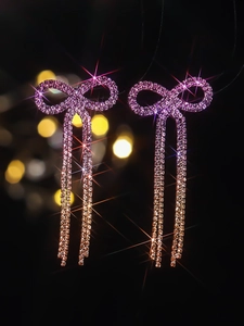 Detail of copper bow earrings featuring long tassels with pink and white rhinestones