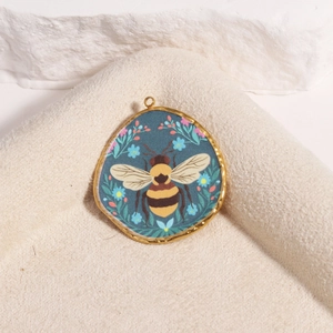Macro detail of golden oval bee and flower enamel pendant on a textured stone base