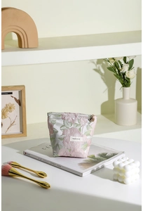 Détail d'une trousse à maquillage en jacquard avec fermeture dorée et pendentif fleurie