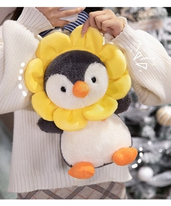 Detail of plush penguin toy wearing a yellow sunflower hood held in a warm cozy setting