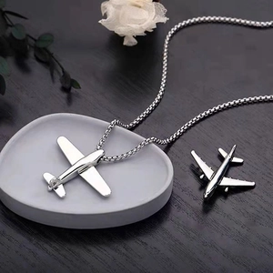 Detailed view of silver airplane pendant necklace and charm on a vintage gray tray