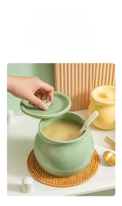 Detail of mint green ceramic seasoning jar with lid and spoon on a woven mat