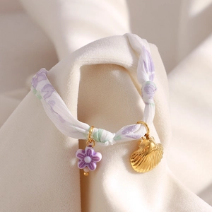 Detail of purple floral fabric strap with gold seashell and flower charm on soft velvet