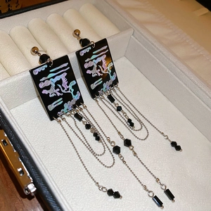 Detail of long tassel earrings with laser-etched black plates and silver chain fringe