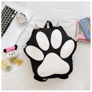 Flat lay of a cute black cat paw backpack with soft 3D details and school accessories