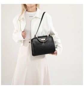 Close-up of black crocodile pattern handbag with golden deer charm and ring handle