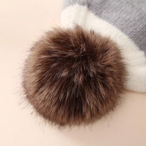 Detail showing a fluffy brown faux fur pom-pom on the top of a grey knit winter beanie