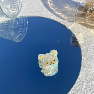 Gros plan d'une pince à cheveux ours bleue marbrée avec reflet sur une surface miroir