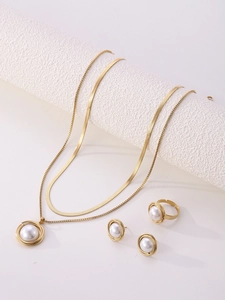 Macro shot of gold-plated jewelry set with layered necklace, pearl earrings, and open ring