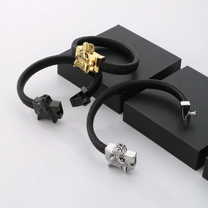 Detail of wolf head charms on black braided leather bracelets in gold, silver, and black