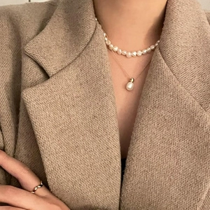 Layered 925 silver necklace with baroque pearls and a gold pendant on a brown wool blazer