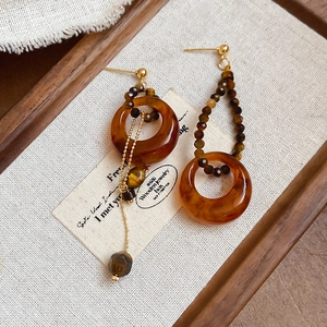 Détail de boucles d'oreilles asymétriques en résine ambrée avec perle œil de tigre et chaîne