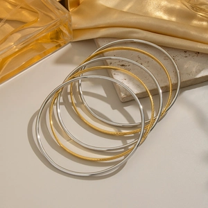Detailed stack of gold and silver stainless steel bangles on minimalist stone background