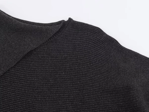 Detailopname van de zwarte geribbelde gebreide textuur op de asymmetrische poncho schouder