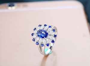 Detailed close-up of a silver ring with an oval blue sapphire and floral petal diamonds