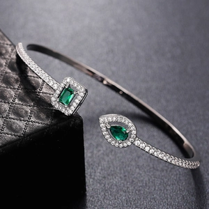 Detail of open bangle with emerald-cut and teardrop green stones on black jewelry box