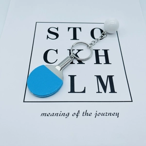 Blue mini table tennis racket keychain with white ball on artistic card background