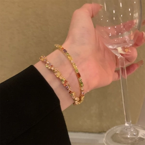 Primo piano di una modella che indossa due bracciali dorati con gemme rettangolari colorate