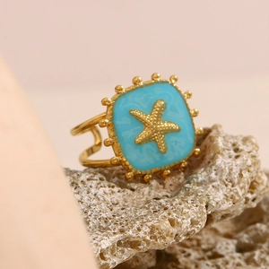 Detailed shot of a gold starfish ring with blue enamel set on a natural rock surface