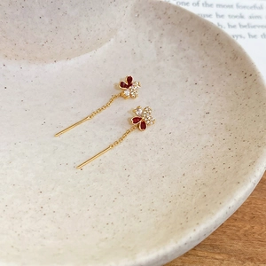 Detail of elegant gold-plated floral earrings with red enamel petals and zircon stones