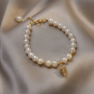 Baroque freshwater pearl bracelet with gold pine cone charm on silk background