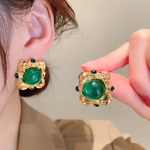 Detail of vintage gold earrings with green gemstones worn on ear and held in hand