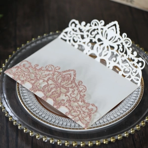 Macro shot of white laser-cut wedding invitation with rose gold glitter on wood surface