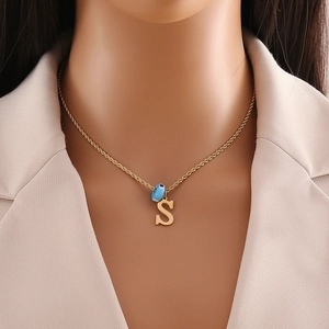 Detail of gold necklace with blue evil eye bead and letter S pendant on a mannequin