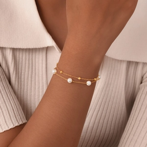 Double-layer golden chain bracelet with white pearls and beads on a female wrist