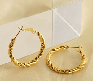 Detail shot of golden twisted hoop earrings on elegant silk background fabric