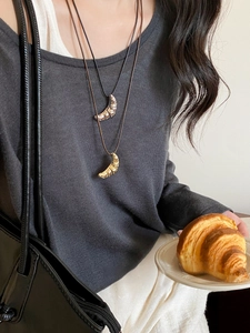 Close-up of layered croissant pendant necklace with black cord on model
