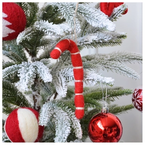 Detail of wool felt candy cane and red ornaments hanging on a snowy Christmas tree branch