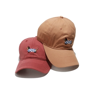 Detail of dachshund embroidery on stack of red and khaki baseball caps with white background