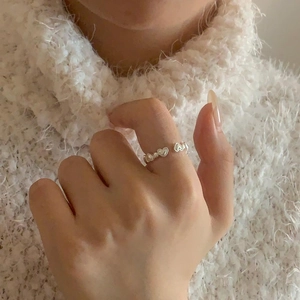 Detailed view of sterling silver hollow heart ring worn on index finger with cozy sweater
