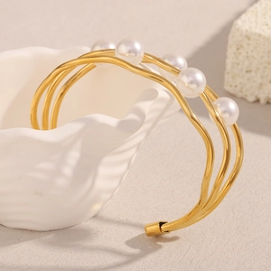 Macro detail of triple-layer gold wave bracelet with five white pearls on shell display