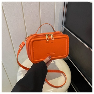 Detail view of orange suitcase-style handbag with top handle and gold hardware zipper
