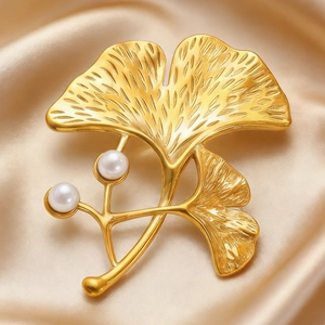 Macro detail of golden ginkgo leaf brooch with elegant pearls on silk fabric