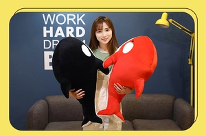 Model holding large black and red plush whale toys to show realistic scale and soft texture