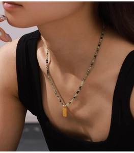 Detail of beaded necklace with green olivine stones and a vertical gold pendant on neck