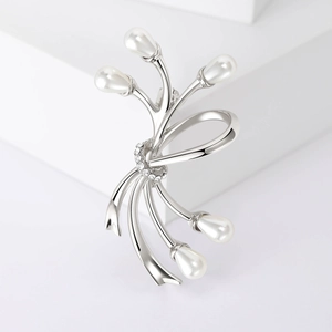 Détail d'une broche nœud argentée avec perles blanches et strass sur support géométrique