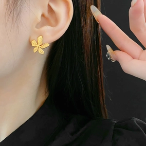 Macro view of gold flower earrings with brushed metal texture on a model's ear