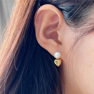Close-up of heart-shaped gold earring with a white pearl on the earlobe