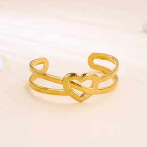 Detail of a gold stainless steel open bangle featuring an elegant textured heart charm