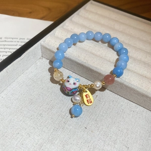 Detail of beaded bracelet with blue gemstones, Maneki Neko charm, and Blessed tag