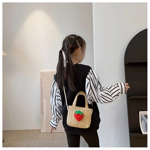 Rear view of a child wearing a beige straw crossbody bag with a 3D strawberry charm