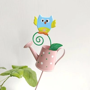 Dettaglio di un paletto da giardino in metallo con annaffiatoio rosa e gufo blu