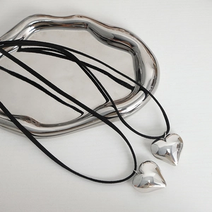 Two retro silver heart pendant necklaces with black adjustable cords on a silver tray