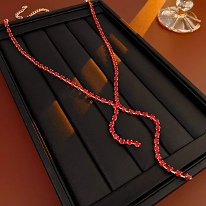 Detailed view of a gold-plated necklace with red teardrop zircon and fringe on a black display