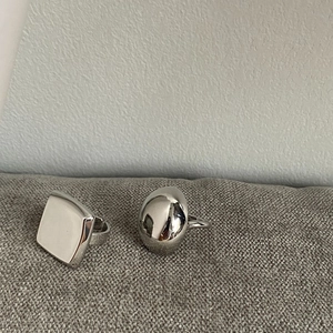 Polished silver geometric square and oval dome rings on textured fabric background